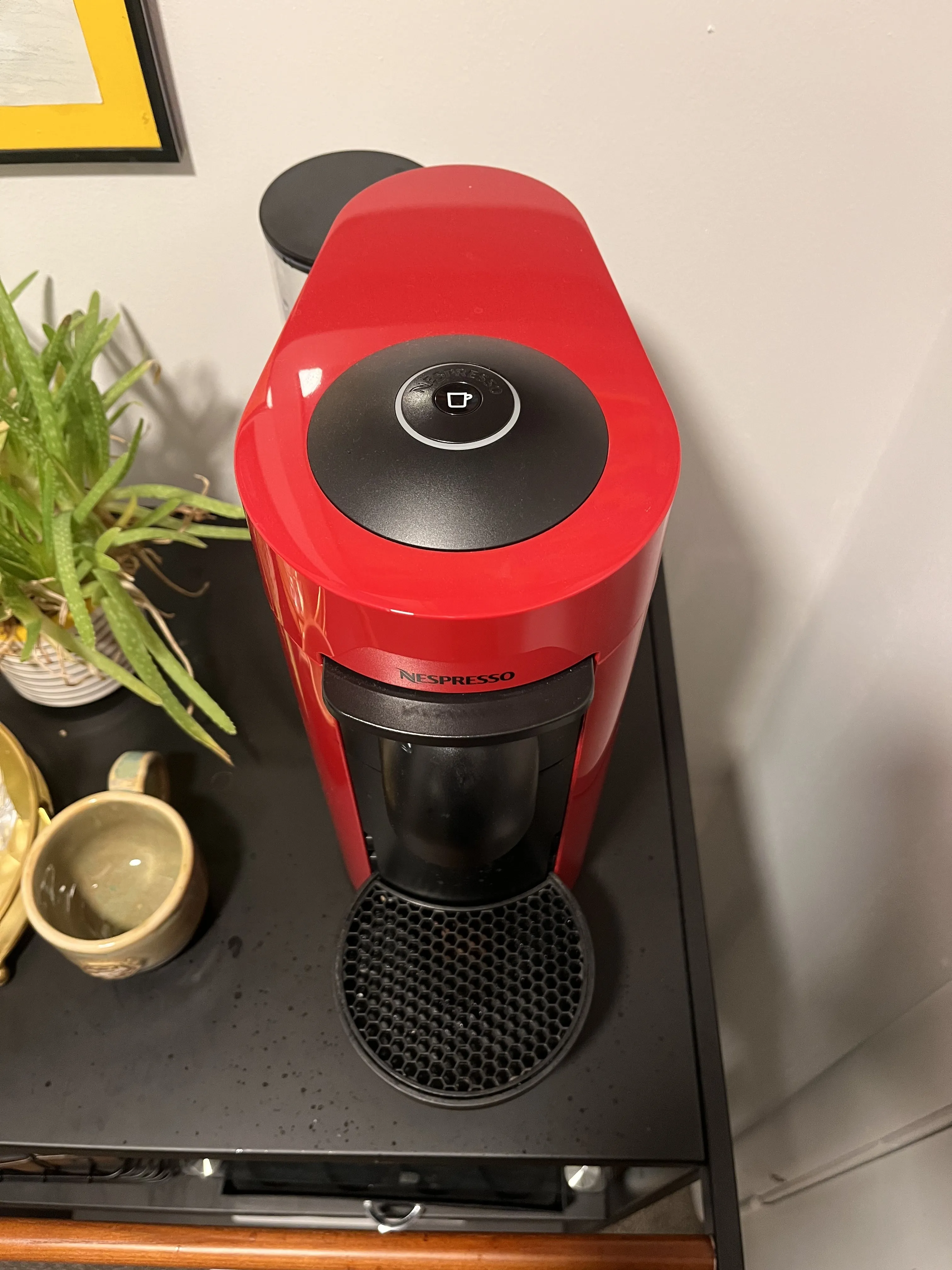 A red Nespresso machine with a single black button and no digital display
